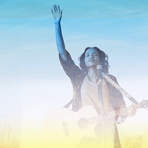 Image of a woman raising hand worshipping with a guitar.