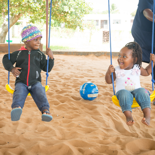 Photo of 2 children (boy and girl) enjoying the new swing set at school